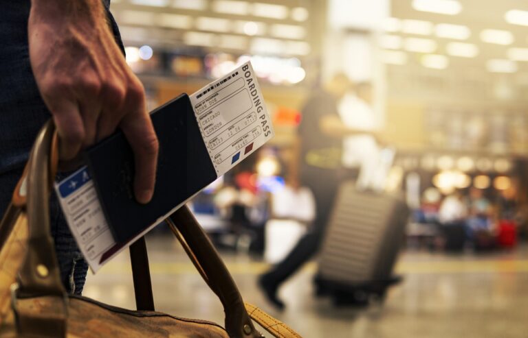Main d'une personne a l'aréoport qui tient un sac et un passeport avec un billet d'embarquement.